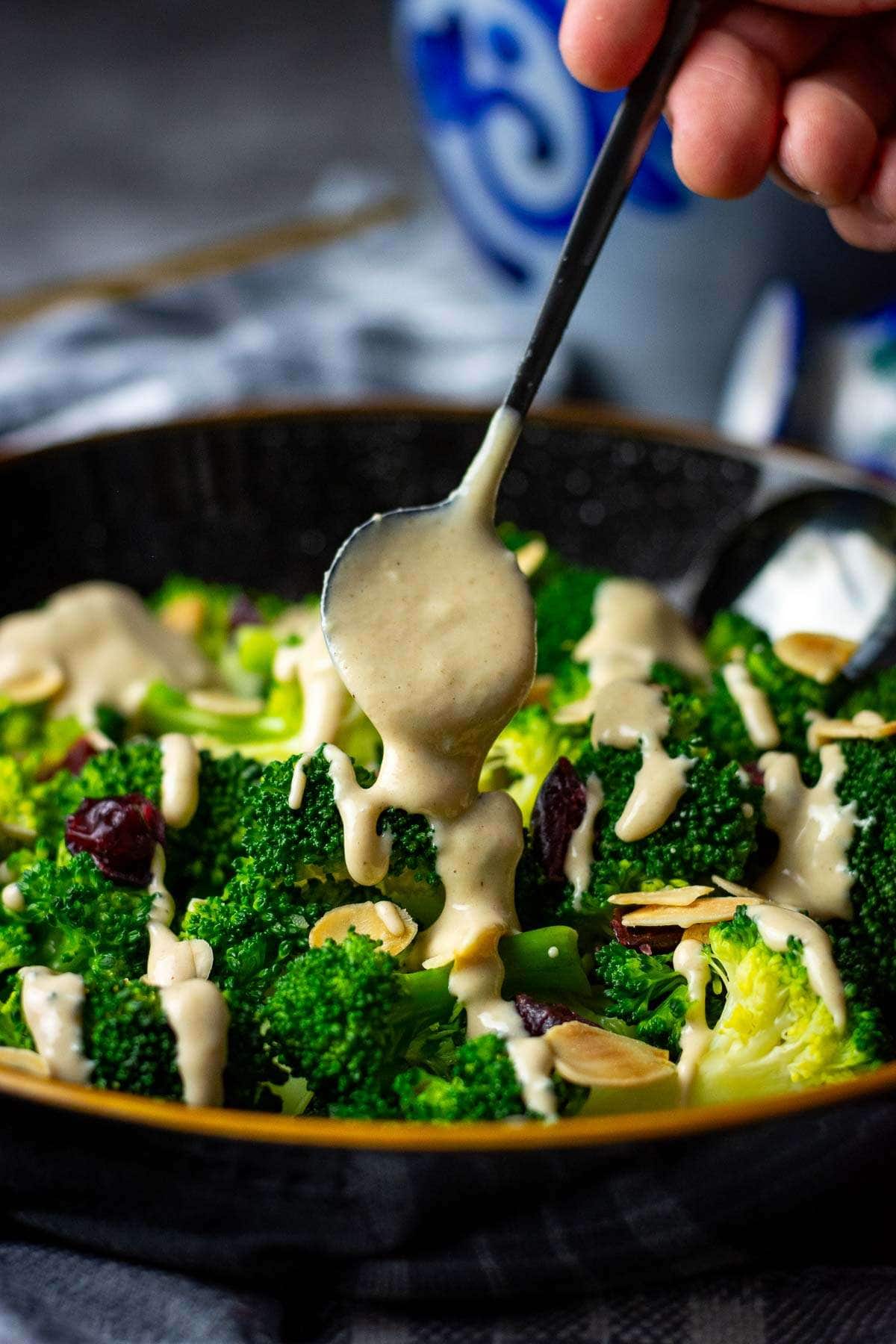 Maple tahini dressing being drizzled over broccoli salad.