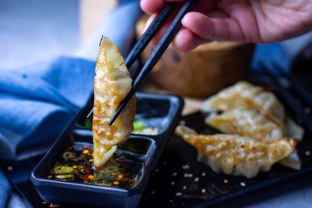 A dipping sauce for gyozas in a small black square bowl.