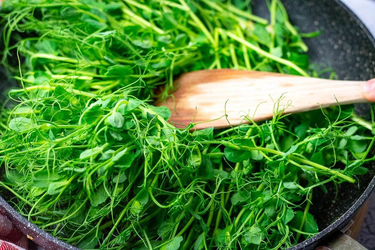 Pea shoots added to the pan with garlic.