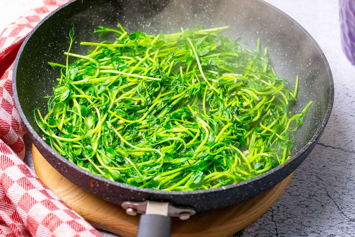 Stir-Fried Pea Shoots in a large frying pan on a wooden board.