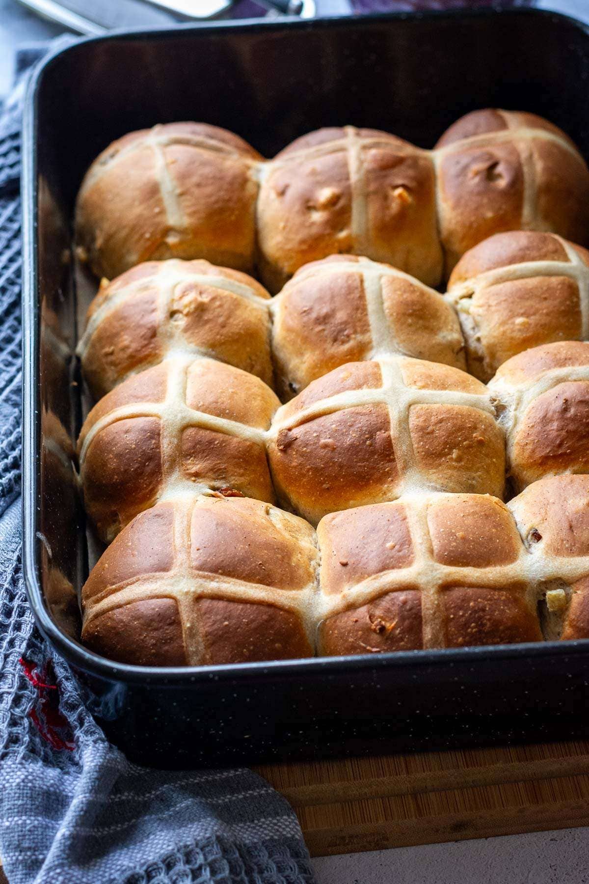Baked sourdough discard Easter buns out of the oven in a black roasting tray.