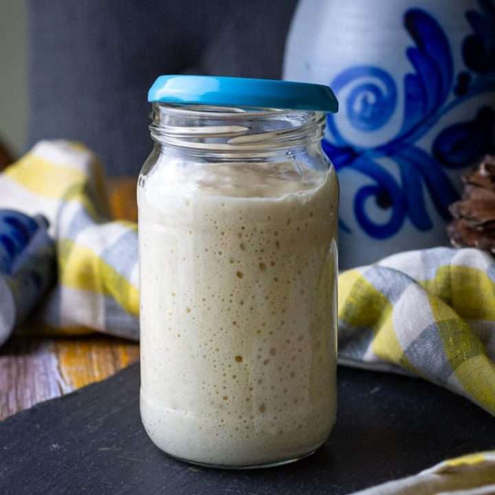 Active and bubbly sourdough starter in a glass jar with a blue lid.