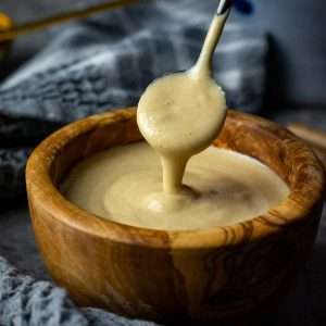 Maple tahini dressing dripping off a small spoon into a wooden bowl.
