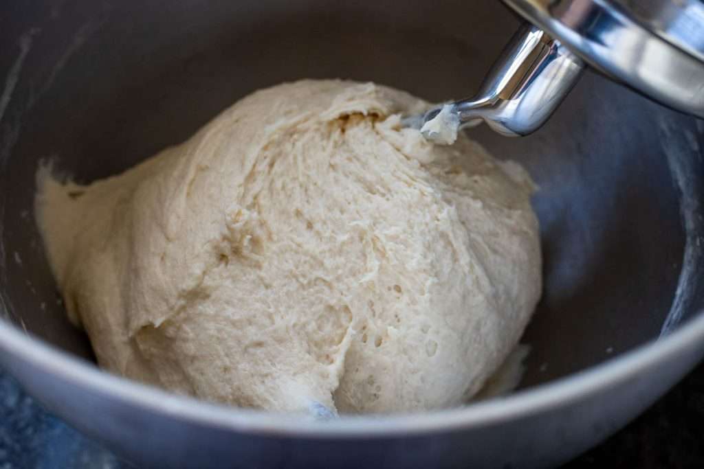 Naan dough wrapping around the dough hook attachment in a stand mixer bowl.