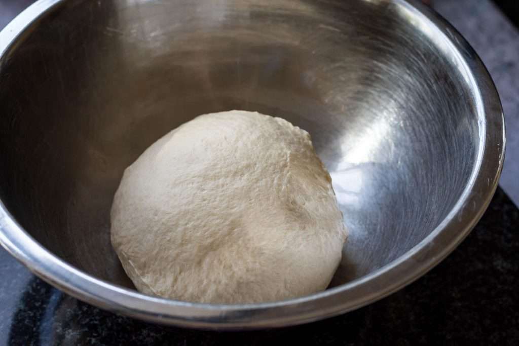 A dough ball before proofing in a metal bowl.