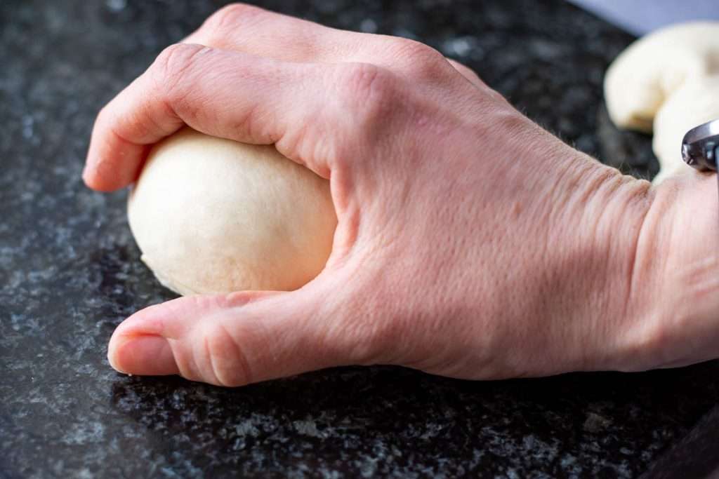 A dough piece being shaped into a tight ball with the palm of the hand.