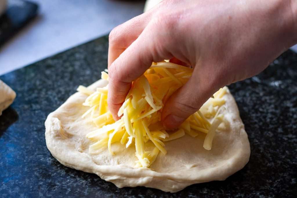 Addinf grated cheese into the centre of stretched out naan dough.