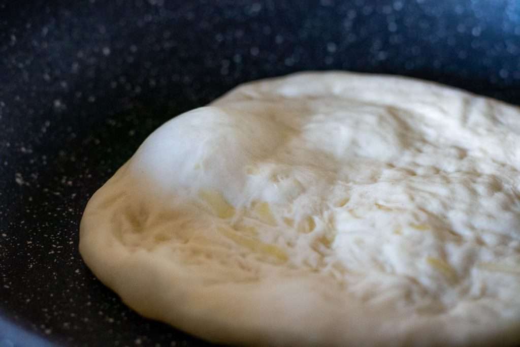 Cheese garlic naan being cooked in a large pan.