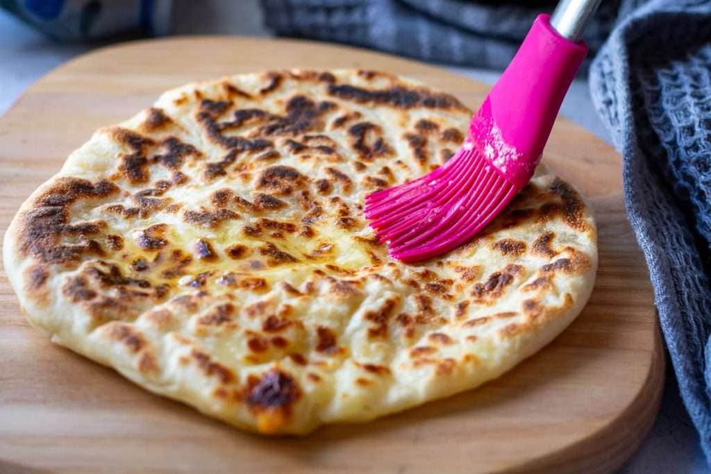 Brushing Cheese garlic naan with butter with a pink pastry brush.