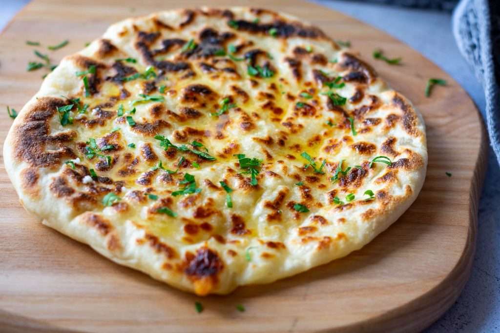 Cheese garlic naan on a wooden board.
