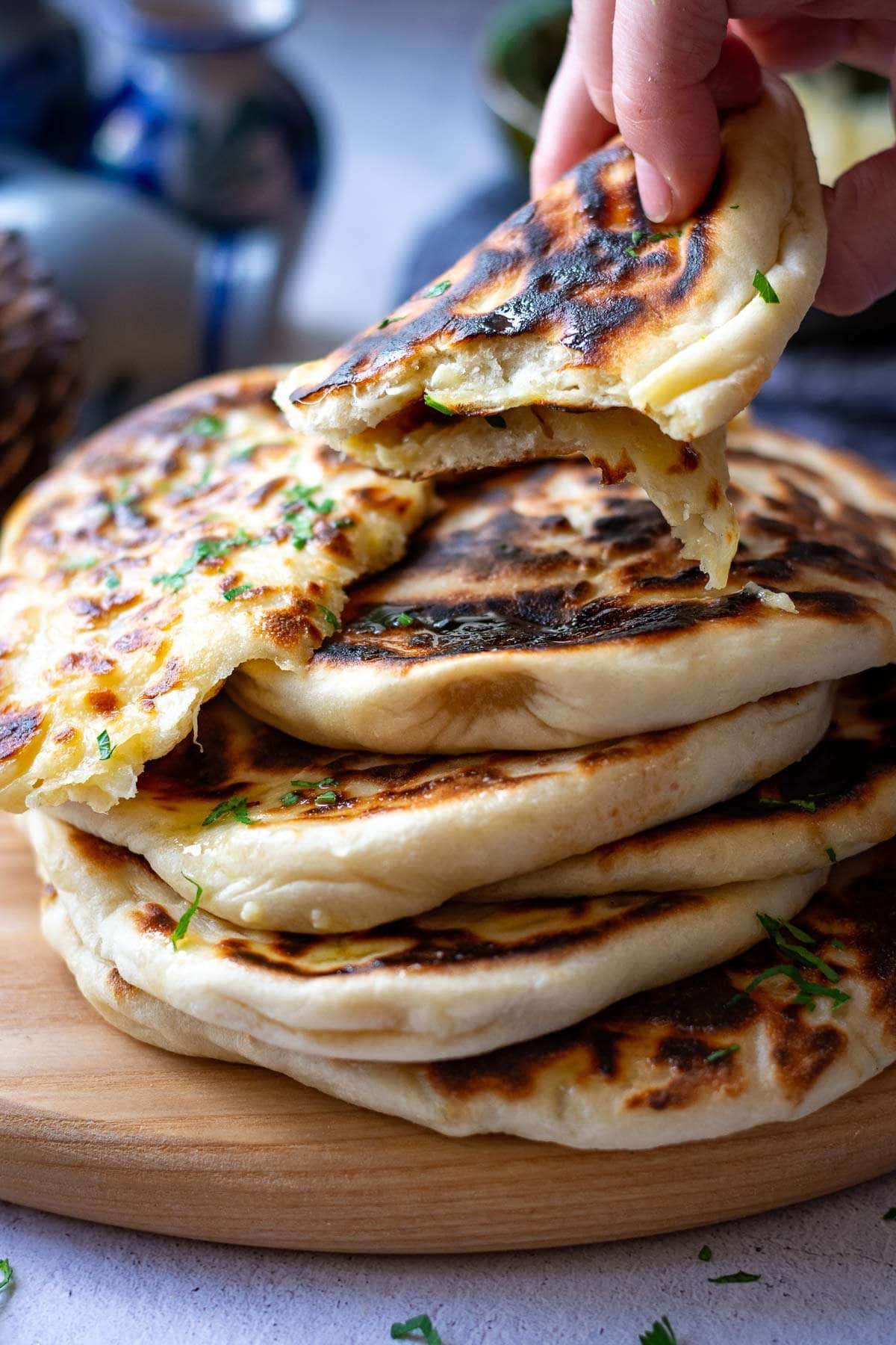 A piece of garlic cheese naan being picked up from a stack of flatbreads.
