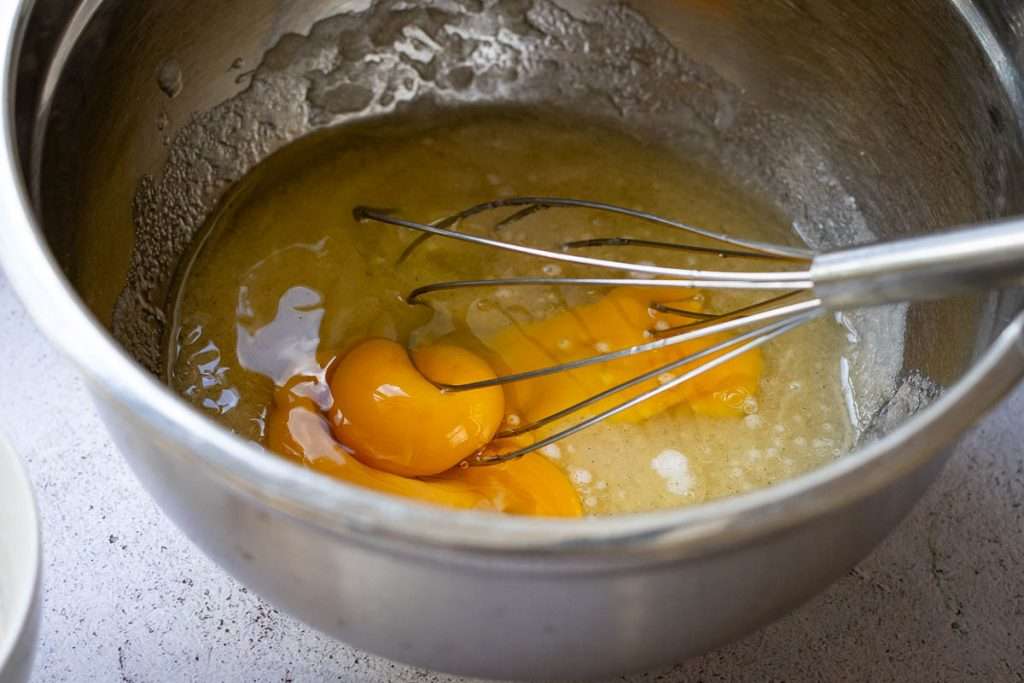 Sugar, oil, egg and vanilla being whisked in a large metal bowl.