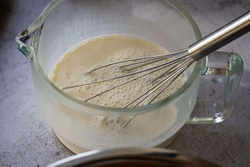 Sourdough discard and milk being whisked in a small glass jug.