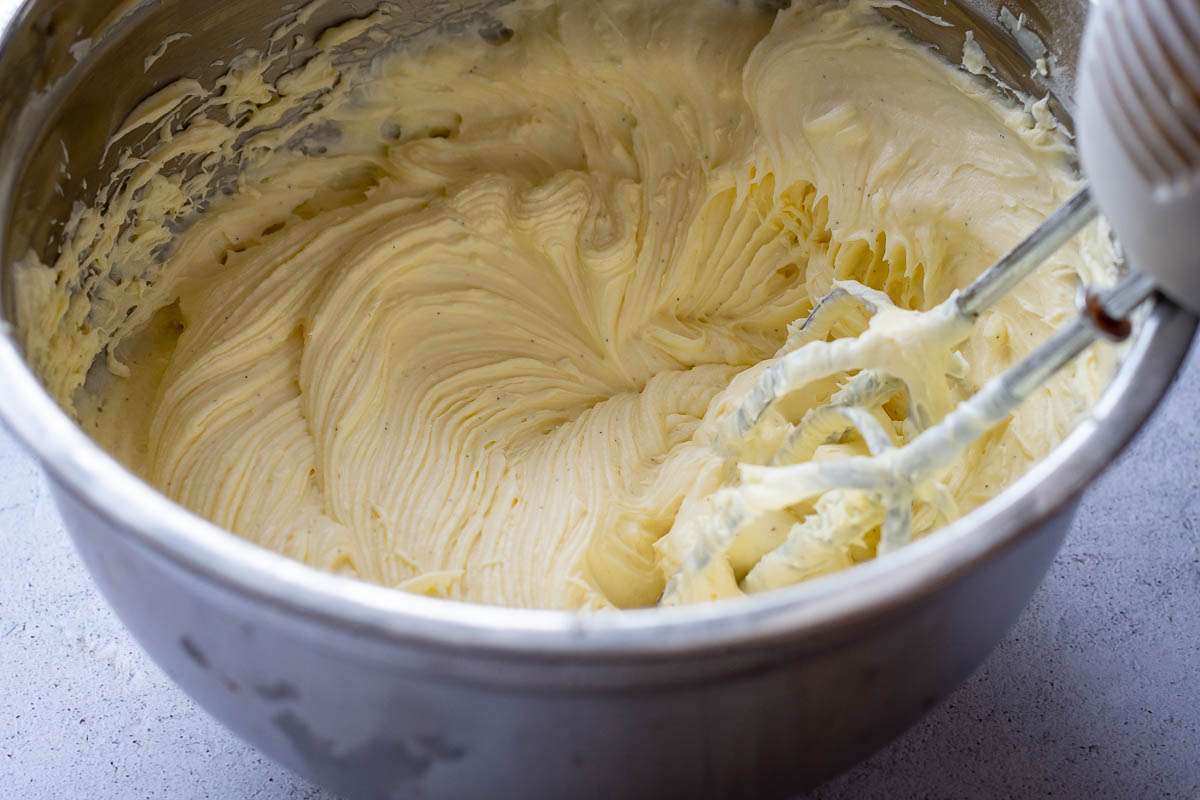 Beating vanilla cream cheese frosting with an electric handheld mixer.
