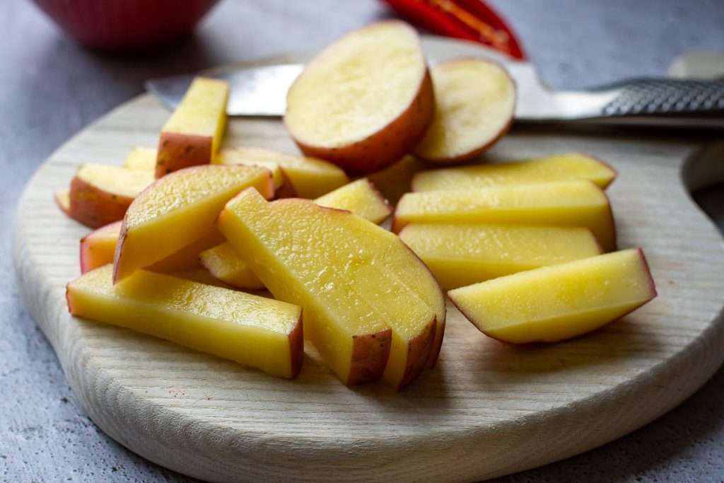 Red potatoes being cut into chips.