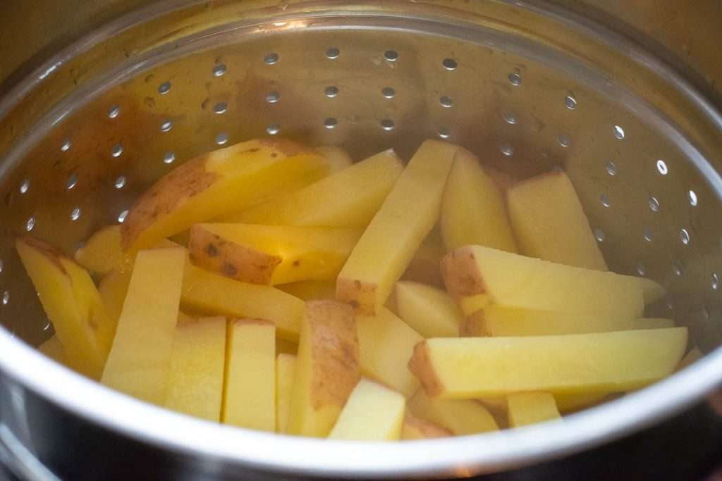 Potato chips steaming in a large colander.