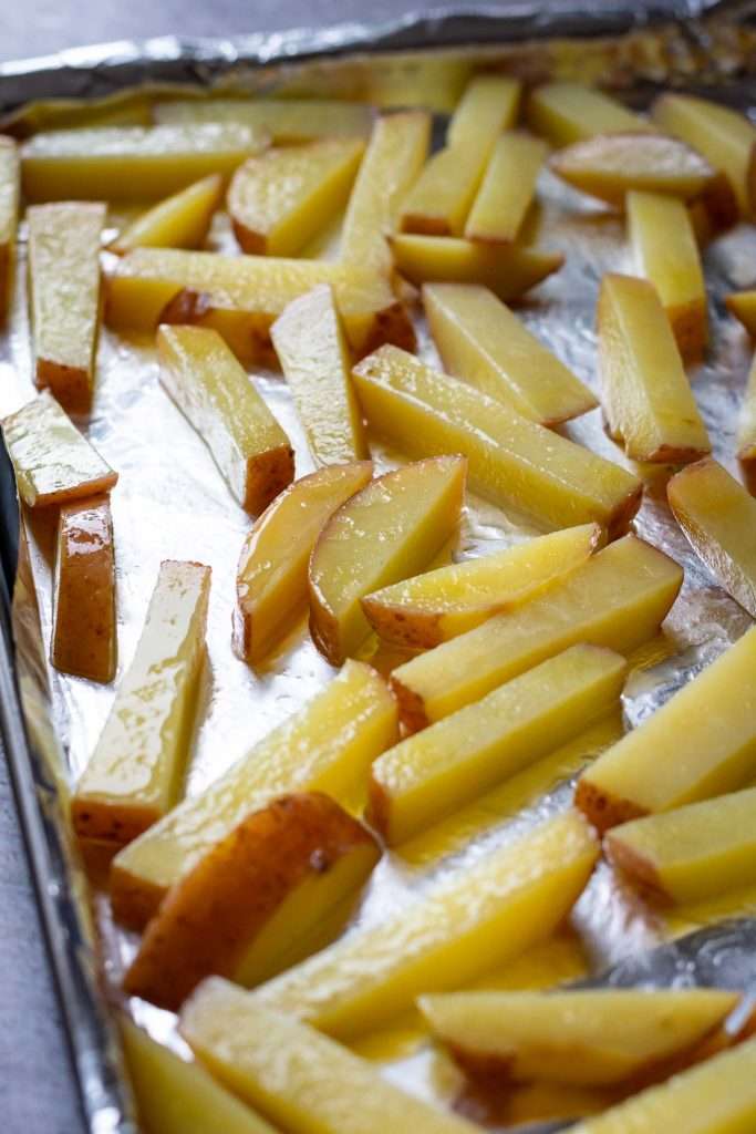 Parboiled potato chips arranged on a large baking tray lined with aluminium foil.