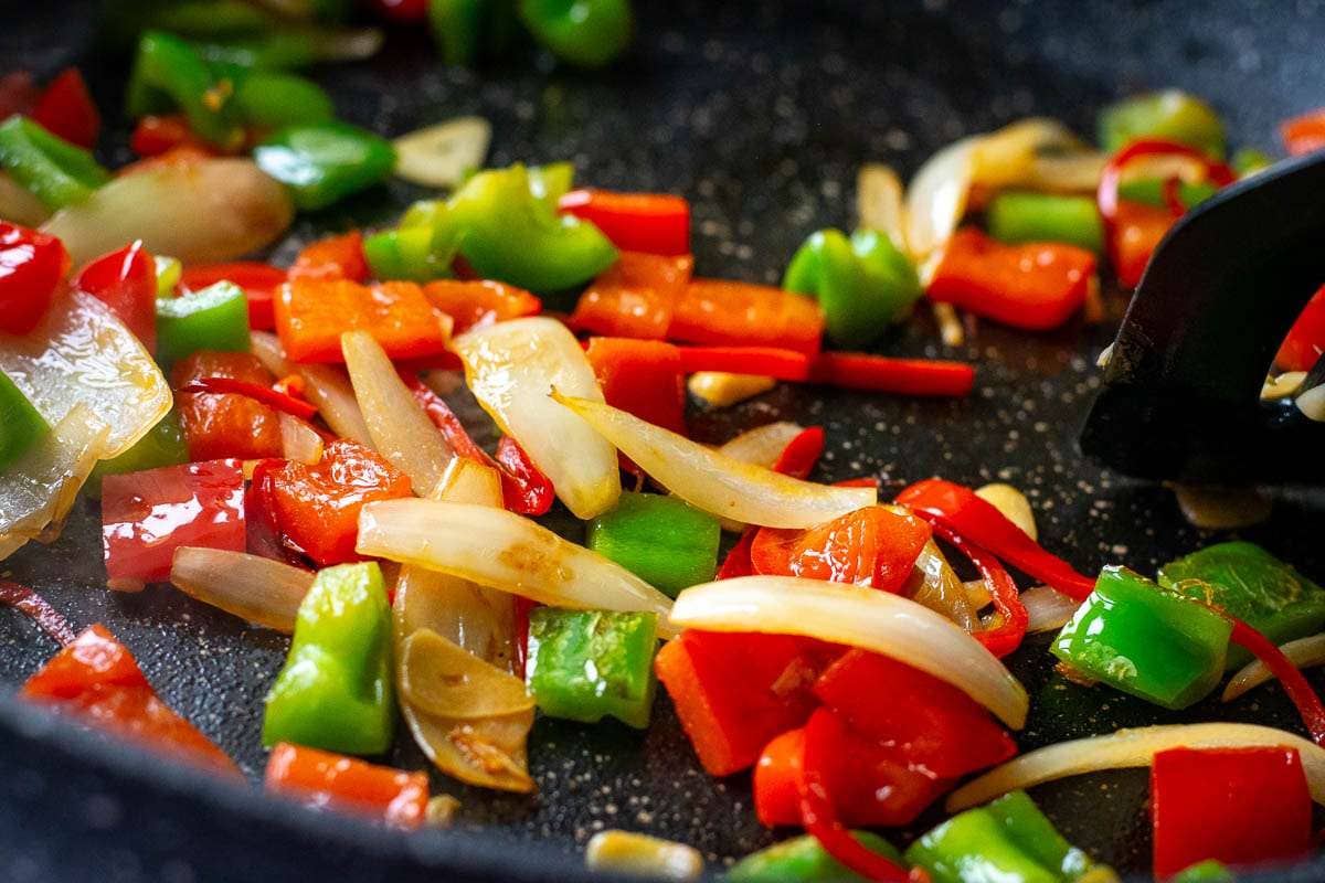 Aromatics, onions and bell peppers frying in a large frying pan.
