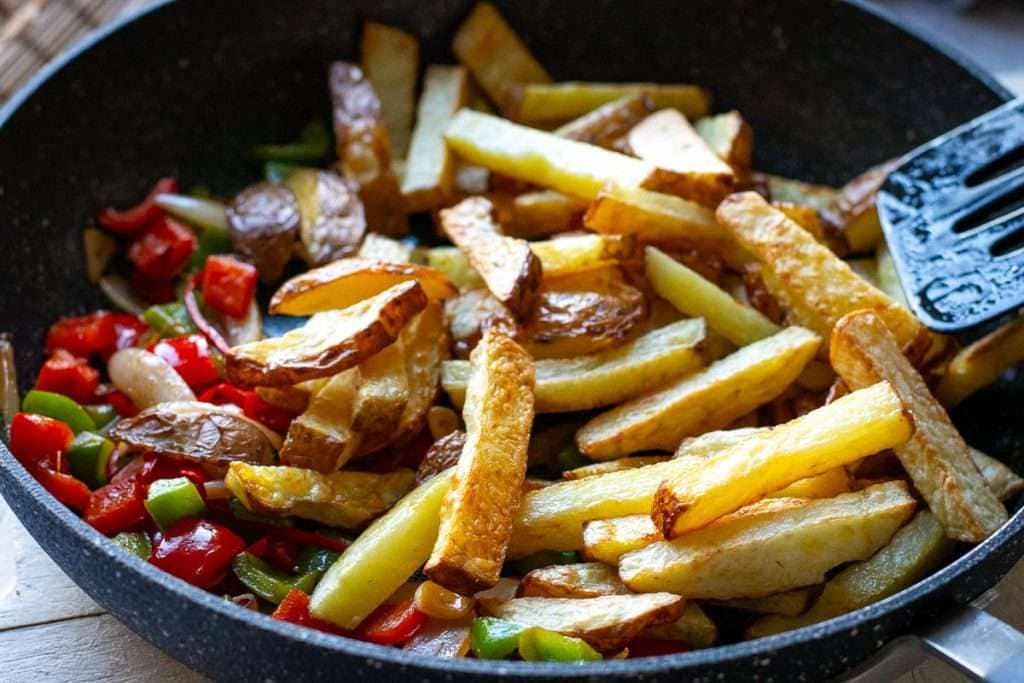 Cooked chips being added to the pan with stired fried veggies.