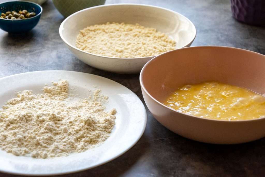 Three bowls: one with beaten egg, another with flour, and the last one with breadcrumbs.