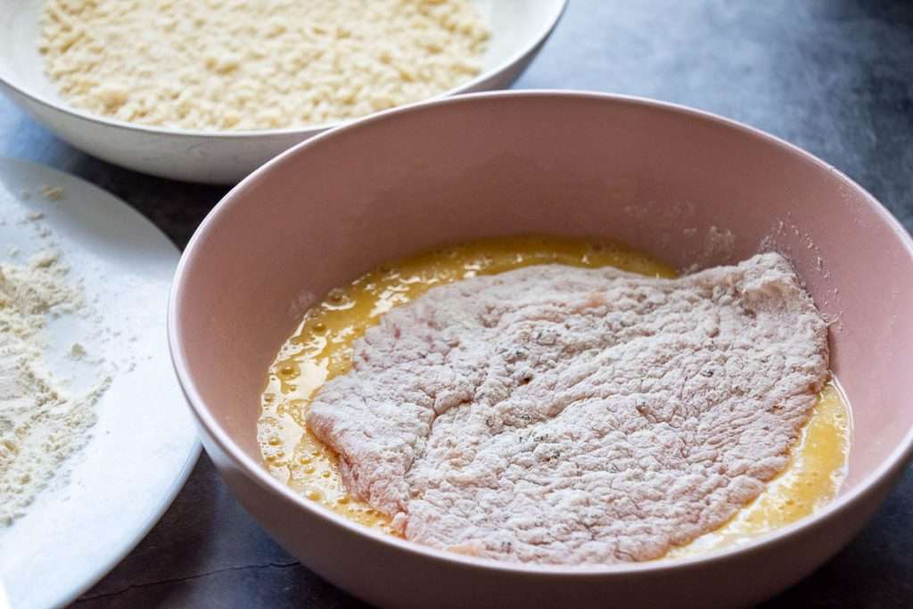 Floured chicken breast in a bowl with an egg.