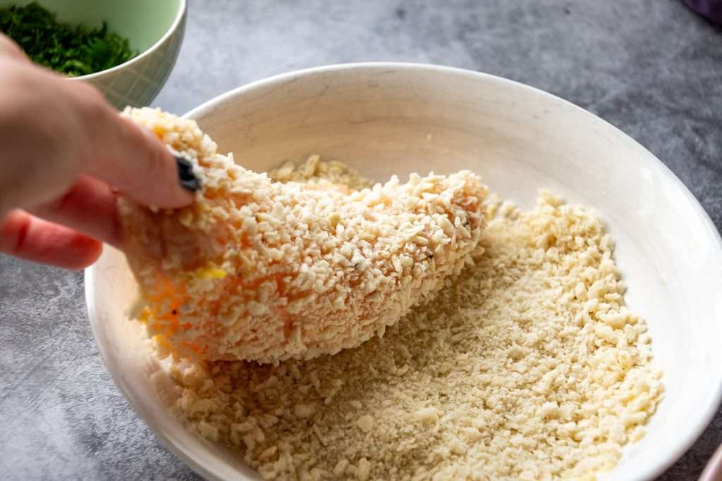 Chicken being coated in breadcrumbs.