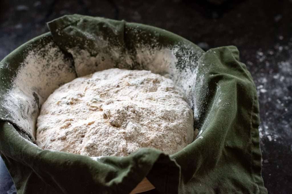 Seeded sourdough in a floured teatowel lined bowl.