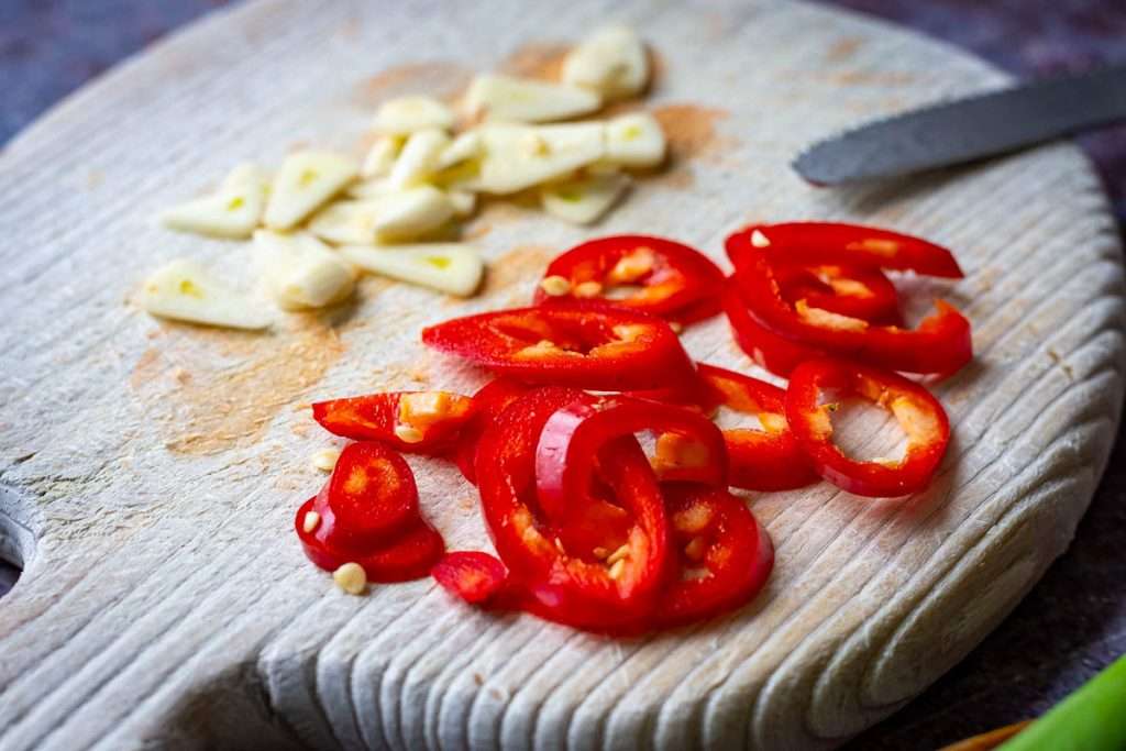 Sliced garlic and red chilli pepper on a wooden chopping board.