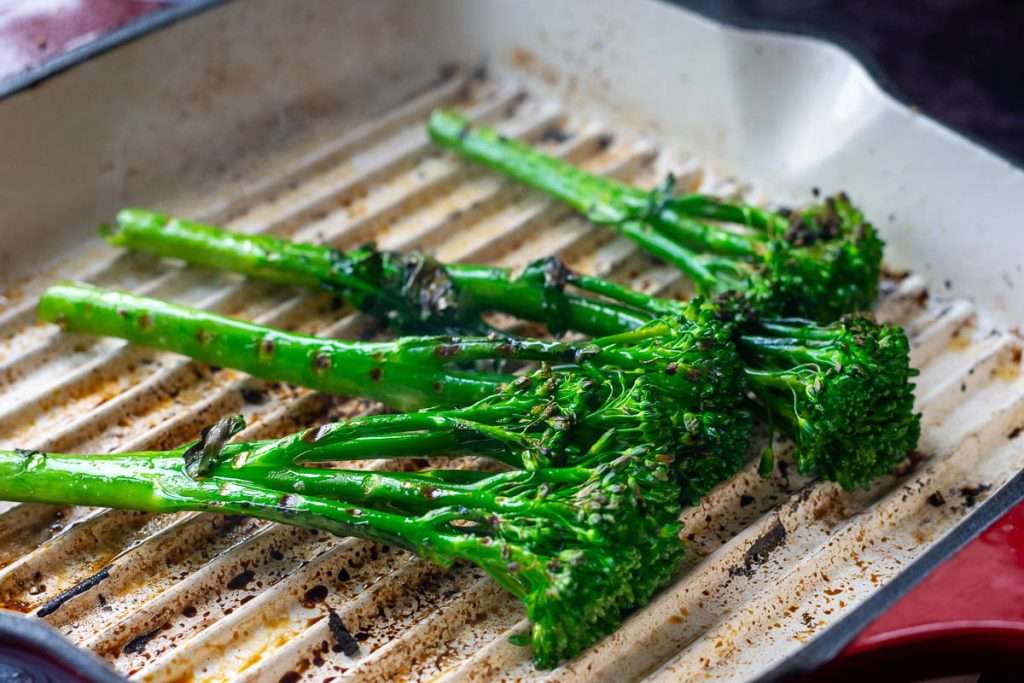 Chargrilled tenderstem broccoli with charred edges in a white griddle pan.