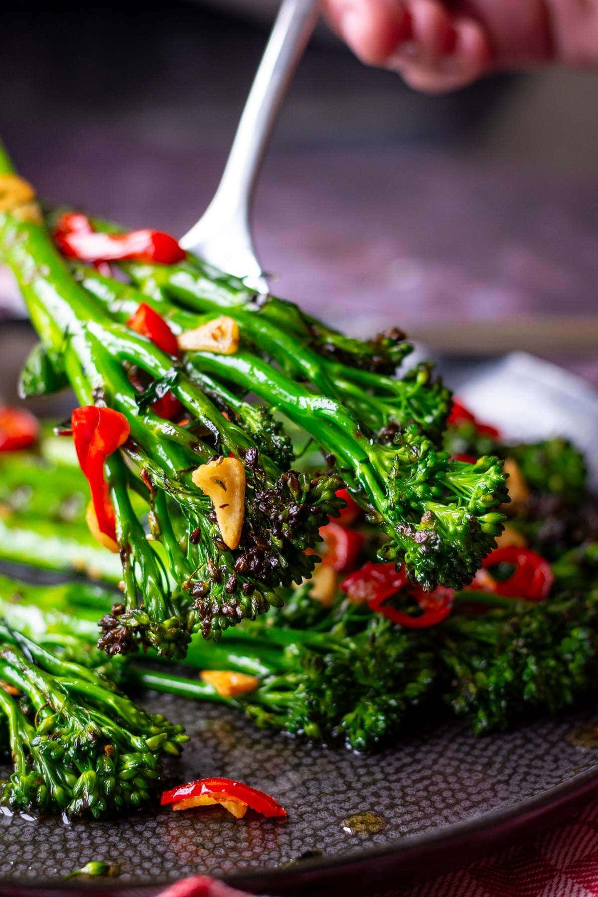 Grilled tenderstem broccoli with chilli and garlic being placed on a black plate.