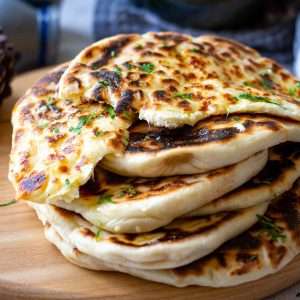A stack of garlic and cheese naan breads on a wooden board.