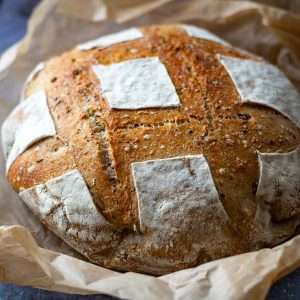 Seeded sourdough bread loaf on a large piece of baking parchment paper.