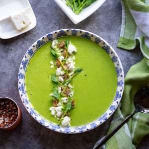 Green pea soup with feta, croutons and pea shoots on top.