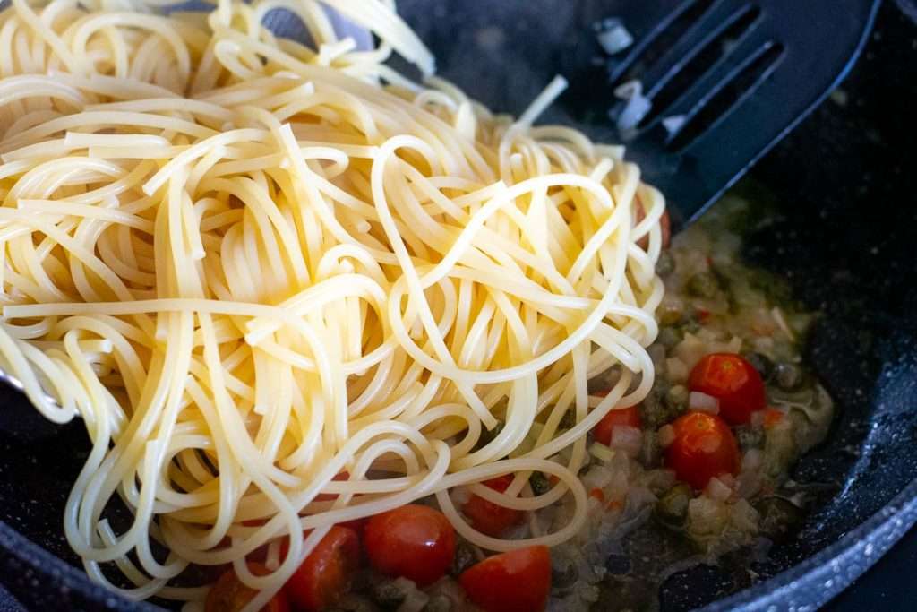 Adding cooked spaghetti to the sauce pan.