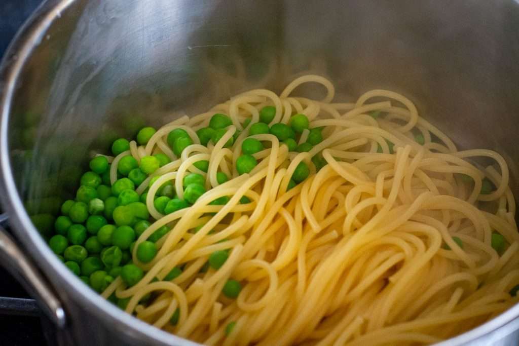 Cooked spaghetti and green peas in a large pot,