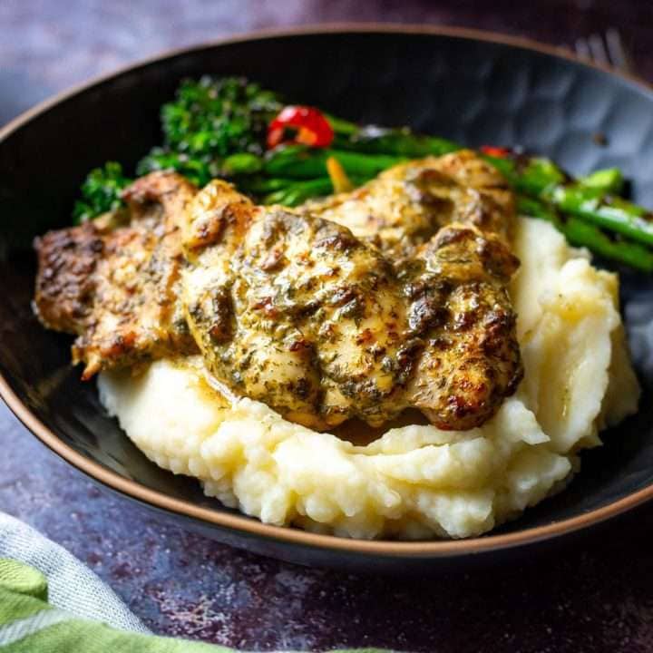 Dill and Dijon Mustard Baked Chicken Thighs on a bed of mashed potatoes in a black bowl.