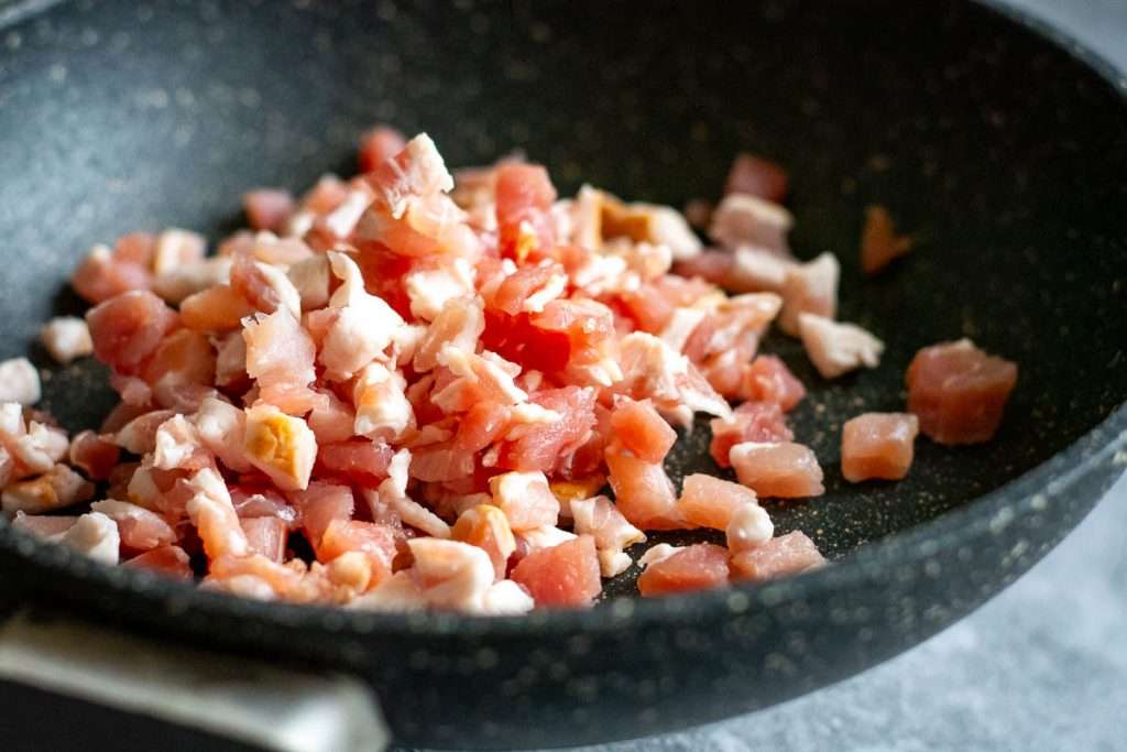 Small bacon cubes in a frying pan.