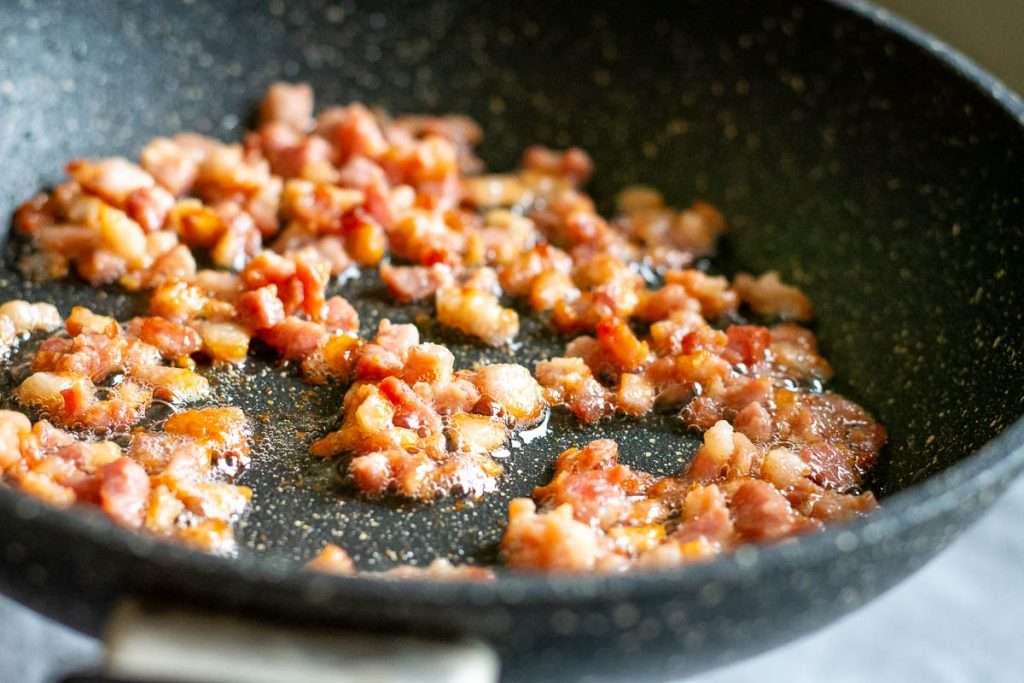 Crispy browned bacon pieces in a frying pan.