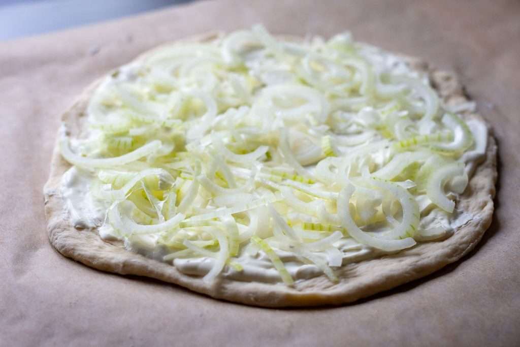 Pizza base with sour cream topped with onion slices.
