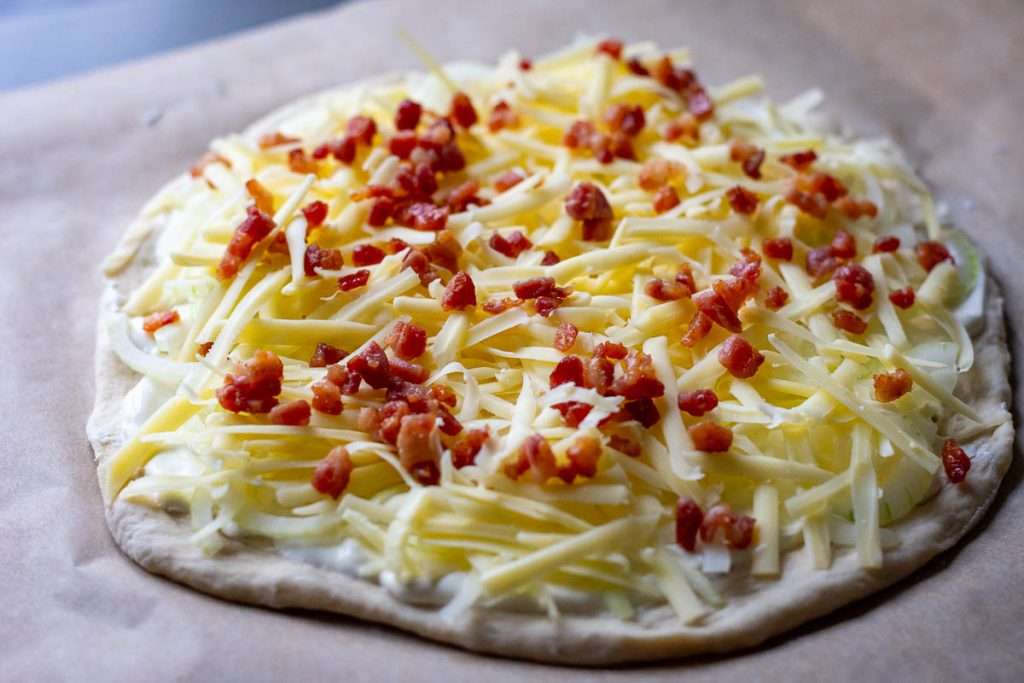 Flamkuchen with onion and bacon assembled and ready to bake.
