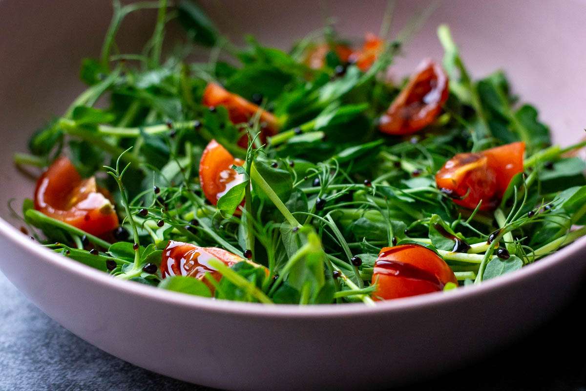 Pea shoot, tomato and balsamic salad in a pale pink bowl.
