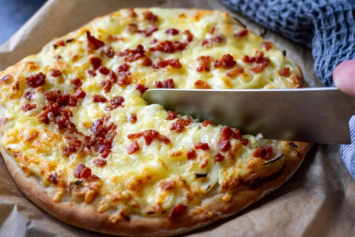 Sour cream pizza with onion and bacon on a large sheet of parchment paper baing cut into slices.