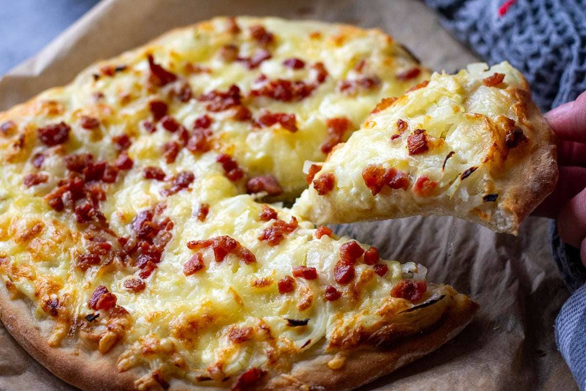 A slice of flammkuchen pizza being pulled out.