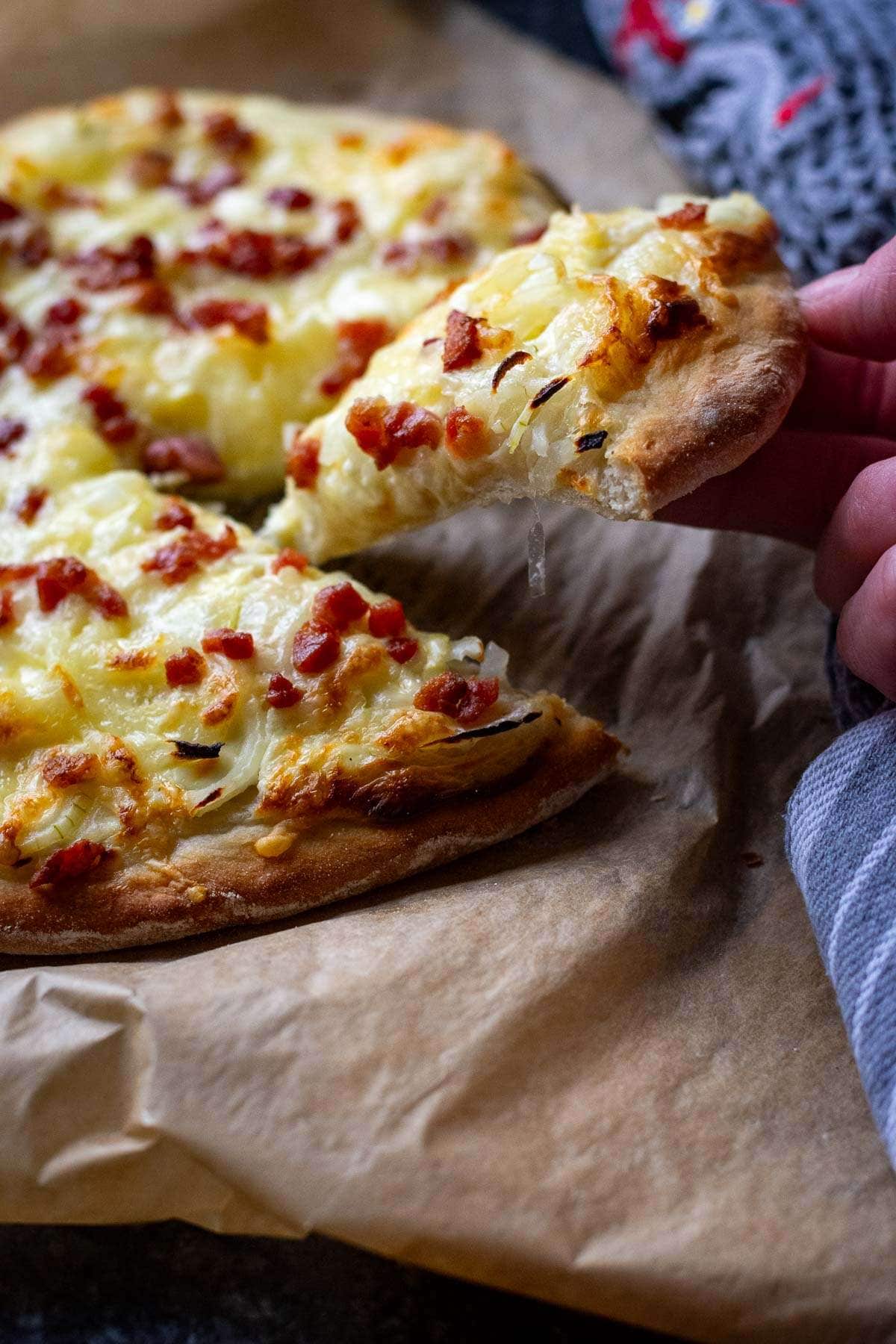 A slice of flammkuchen pizza being pulled out.
