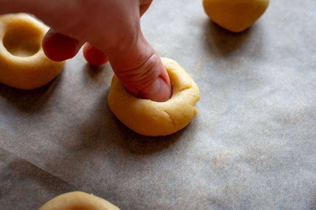 Pressing a thumb into the cookie dough ball to create a thumbprint.