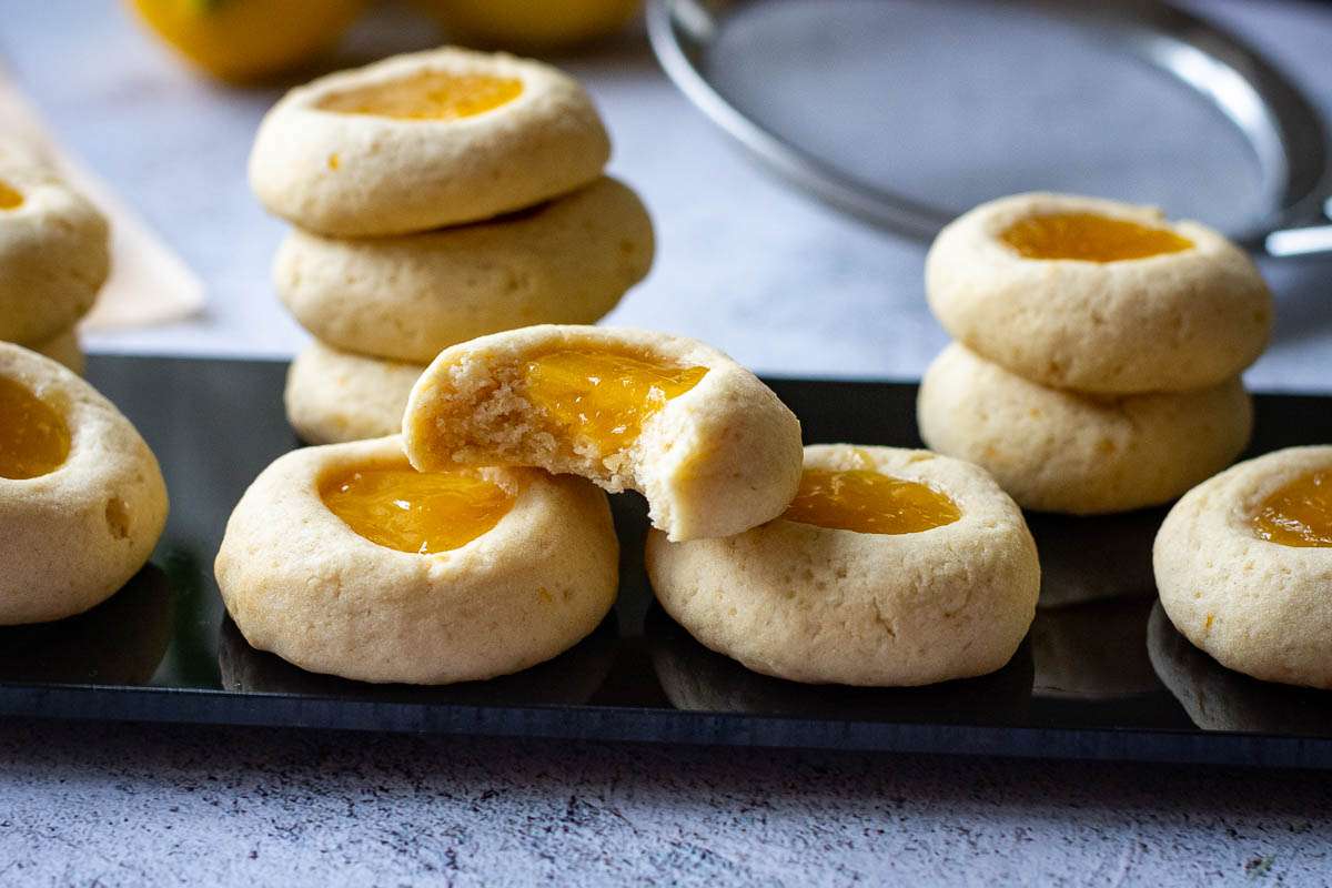 Lemon Thumprint Cookies With Lemon Curd on a black board with one cookie having a bite mark.