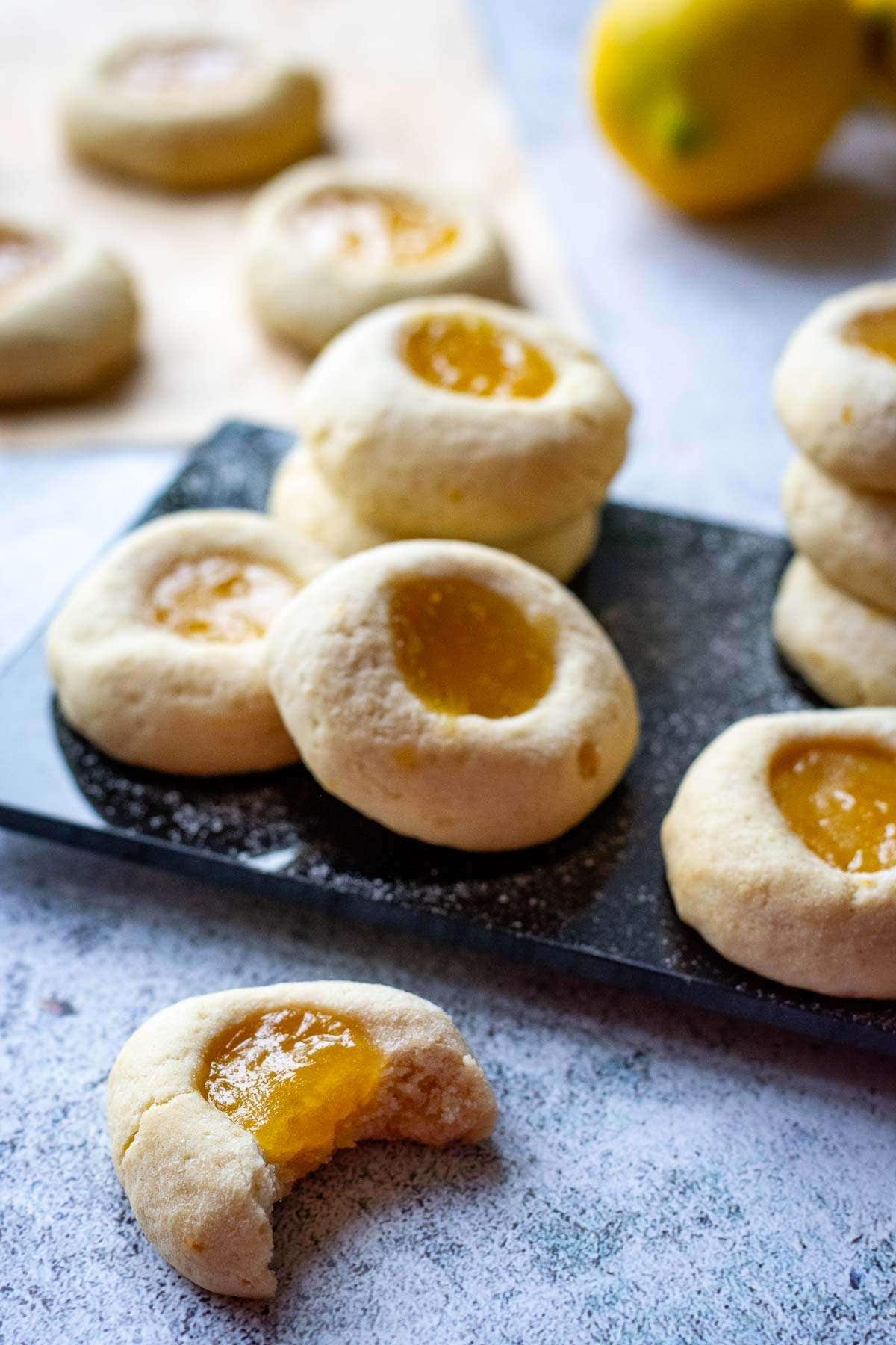 Lemon Thumprint Cookies With Lemon Curd on a black board with one cookie being picked up.