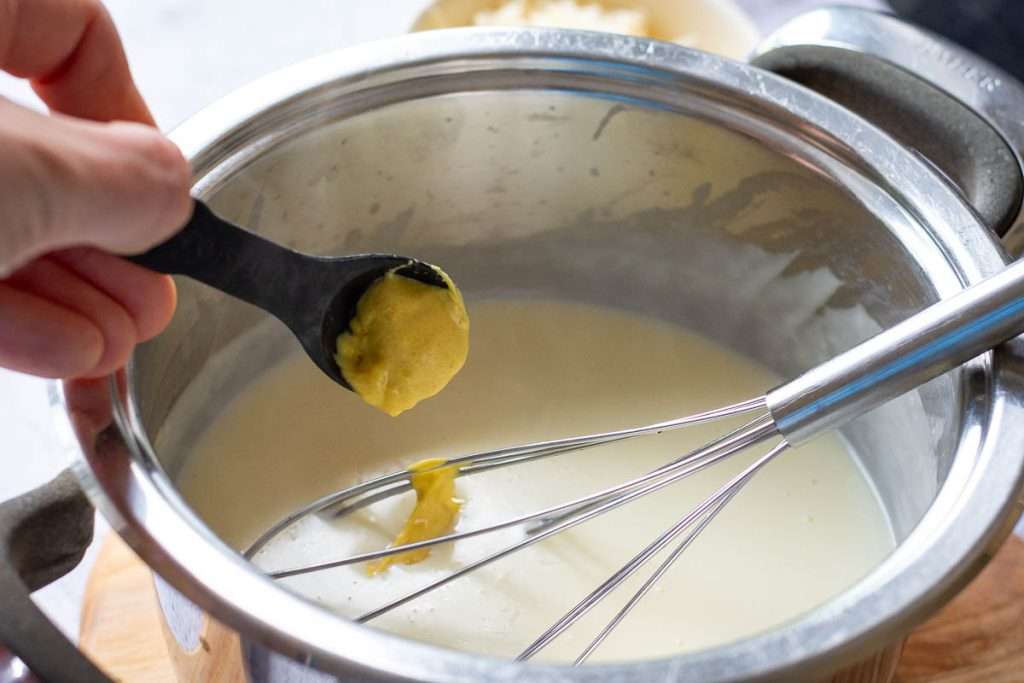 Adding mustard to the white sauce.