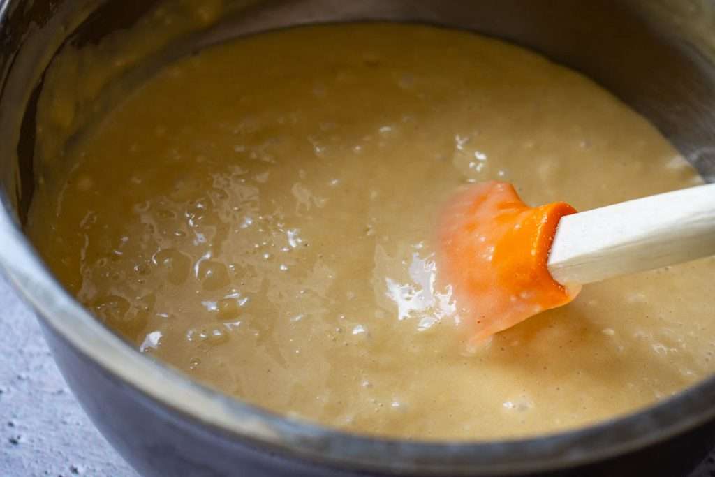 The cake batter ready in a metal bowl with an orange rubber spatula in it.