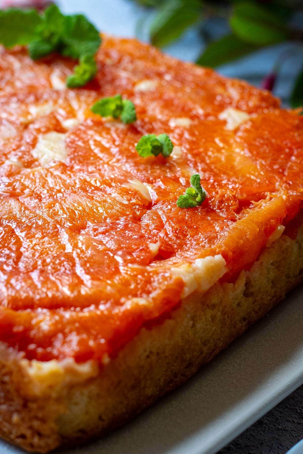 Square grapefruit upsidenown cake on a white plate decorated with mint.